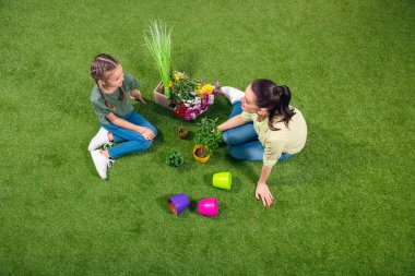mother and daughter with plants and flowerpots sitting on green grass clipart