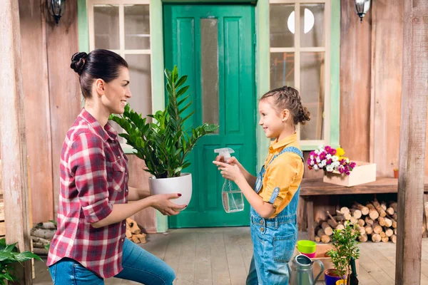 Mother and daughter watering plant with spray bottle, standing on porch — Stock Photo, Image