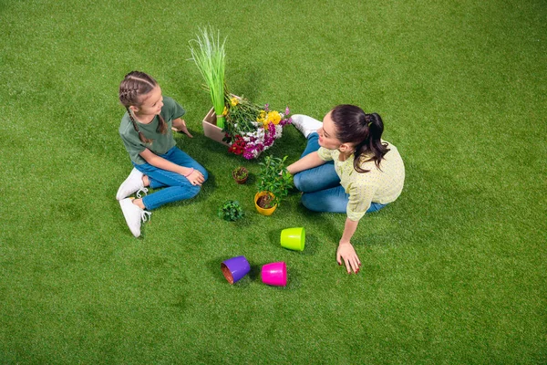 Madre e hija con plantas y macetas sentadas sobre hierba verde —  Fotos de Stock