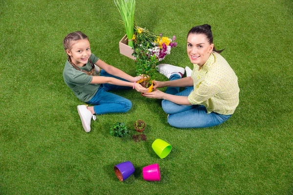 Mère et fille avec des plantes et des pots de fleurs assis sur l'herbe verte — Photo