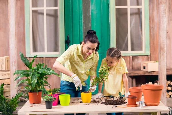 Ibu dan anak perempuan dengan tanaman dan pot bunga berdiri di meja di teras — Stok Foto