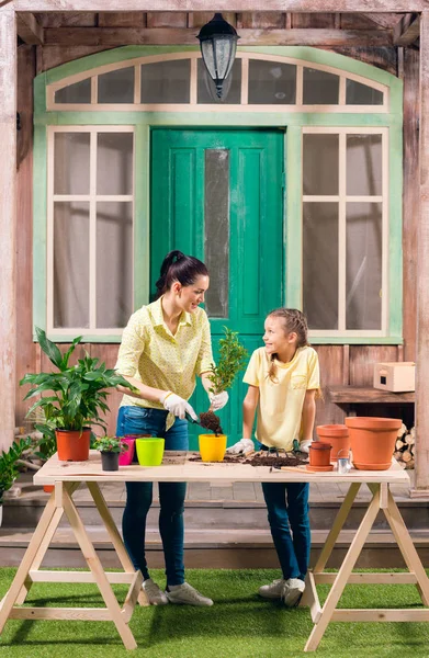 Madre e figlia con piante e vasi da fiori in piedi a tavola sul portico — Foto Stock