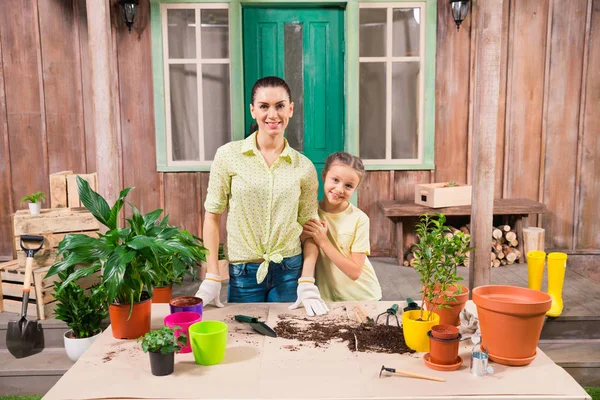 Mère et fille avec des plantes et des pots de fleurs debout à table sur le porche — Photo