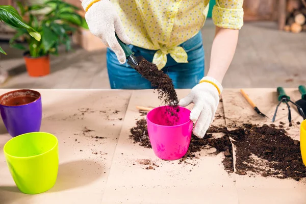 Vue recadrée de la femme avec pelle, terre, pots de fleurs et plante sur la table — Photo