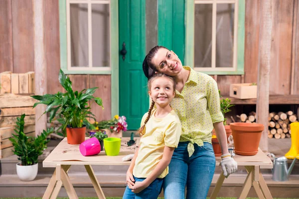 Mãe e filha com plantas e vasos de flores de pé e abraçando à mesa na varanda — Fotografia de Stock