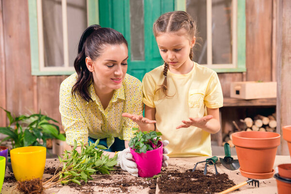 mother and daughter with plants and flowerpots standing at table on porch 