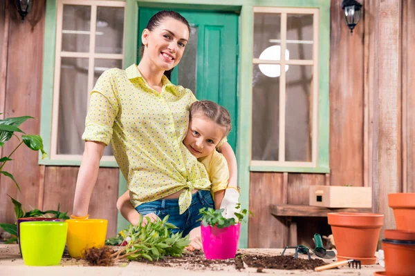 Madre e figlia con piante e vasi da fiori in piedi e abbracci a tavola sul portico — Foto stock gratuita