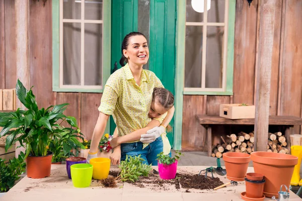 Mère et fille avec des plantes et des pots de fleurs debout et étreignant à table sur le porche — Photo