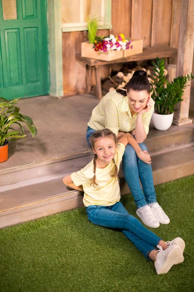 Gelukkig moeder en dochter zitten op de veranda en camera te kijken — Stockfoto