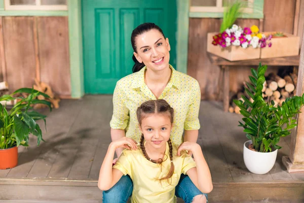 Happy mother and daughter sitting on porch, hugging and looking at camera — Stock Photo, Image