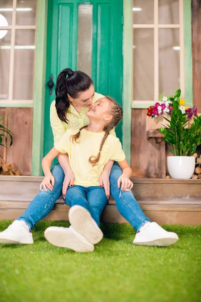 Gelukkig moeder en dochter zitten op de veranda en knuffelen buitenshuis — Gratis stockfoto