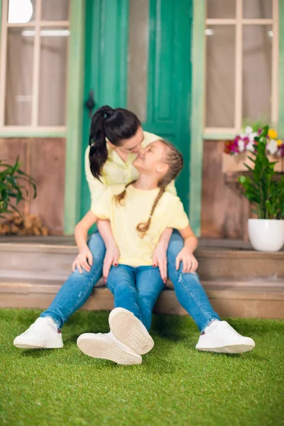 Feliz madre e hija sentadas en el porche y abrazándose al aire libre — Foto de stock gratuita