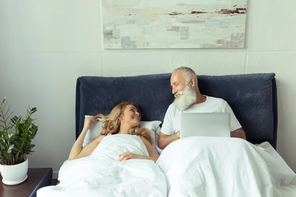 Volwassen paar in bed met laptop — Stockfoto