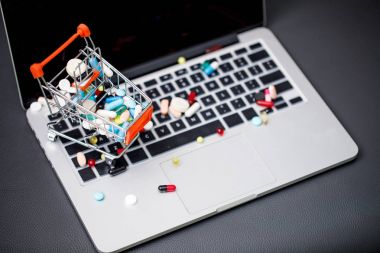 laptop and pills in small shopping trolley clipart
