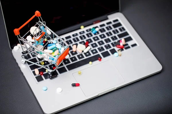 Laptop e pílulas em pequeno carrinho de compras — Fotografia de Stock