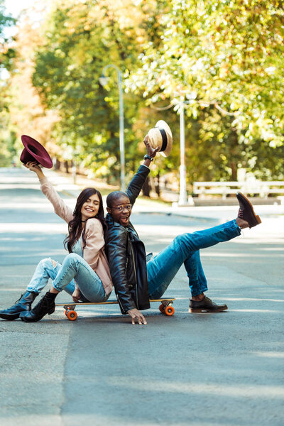 couple sitting on longboard with hats in hands 