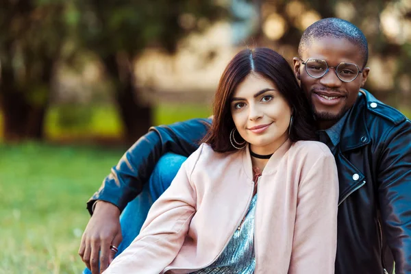 Casal multicultural sentado na grama — Fotografia de Stock