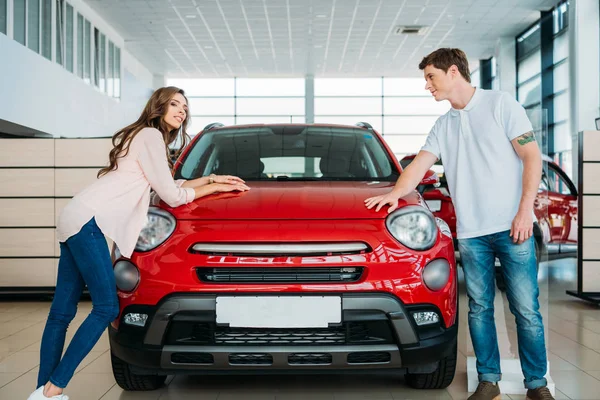 Coppia appoggiata su auto rossa nello showroom — Foto Stock