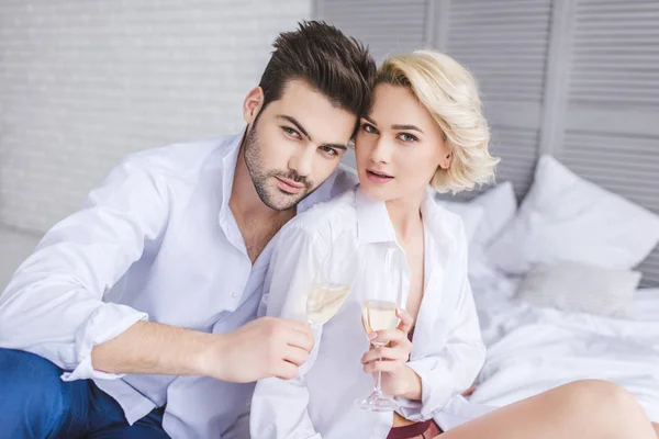 beautiful young couple in white shirts holding glasses of champagne and looking at camera