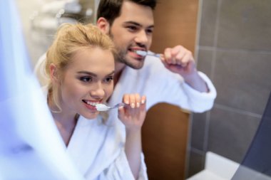 affectionate couple brushing teeth and looking at mirror clipart