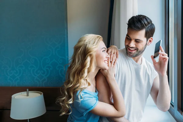 Sonriente Pareja Con Teléfono Inteligente Cerca Ventana Habitación — Foto de Stock