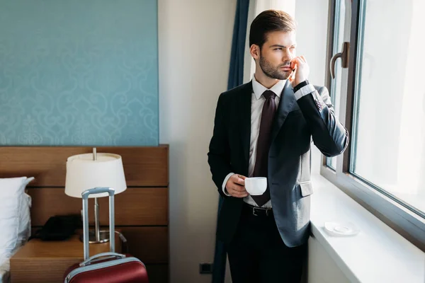 handsome businessman talking by smartphone in hotel room and looking away