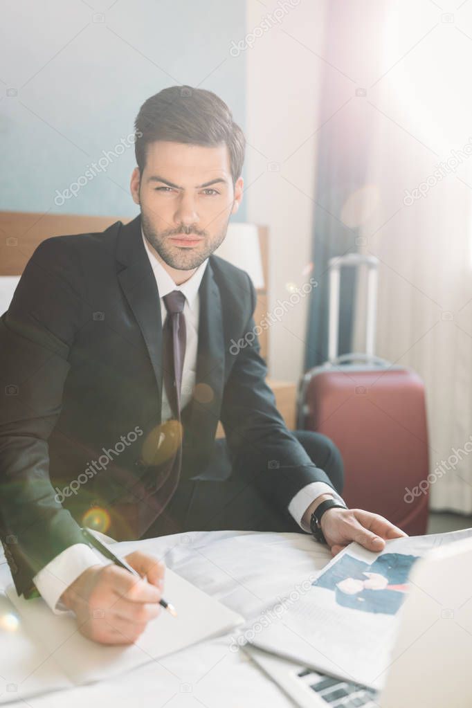 businessman sitting on bed with newspaper and notebook 