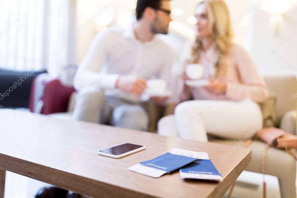 couple holding cups of coffee with smartphone, passports and tickets on foreground