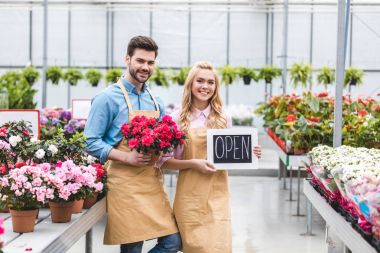 Young man and blonde woman holding Open board by flowers in glasshouse clipart