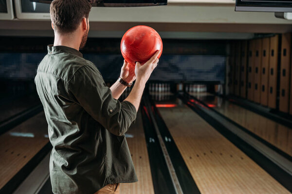 rear view of man with bowling ball looking at alleys