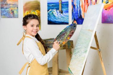Palet tutarak ve kamera Atölye Sanat Okulu bakarak çocuğun
