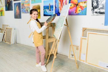 Tuval sanat okulun atölyesinde yakın duran ve kameraya bakarak gülen çocuk