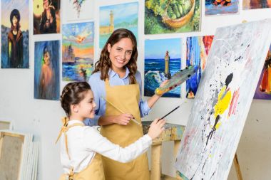 smiling teacher and pupil painting in workshop of art school clipart
