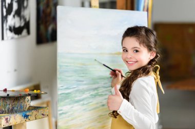 Sanat Okulu atölyede resim ve başparmak gösterilmesini gülümseyen çocuk