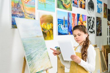 tablet Atölye Sanat Okulu ile ayakta ve tuval üzerine işaret eden çocuk