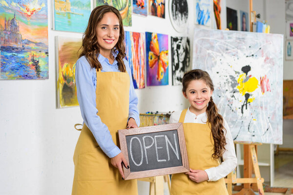 teacher and pupil holding signboard with word open in workshop of art school