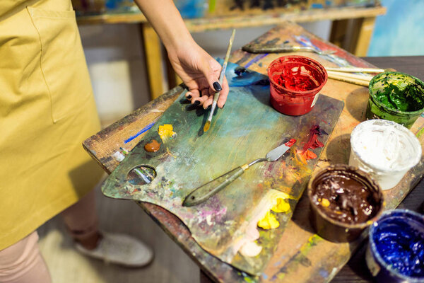 обрезанное изображение художника, держащего кисть над палитрой в мастерской
