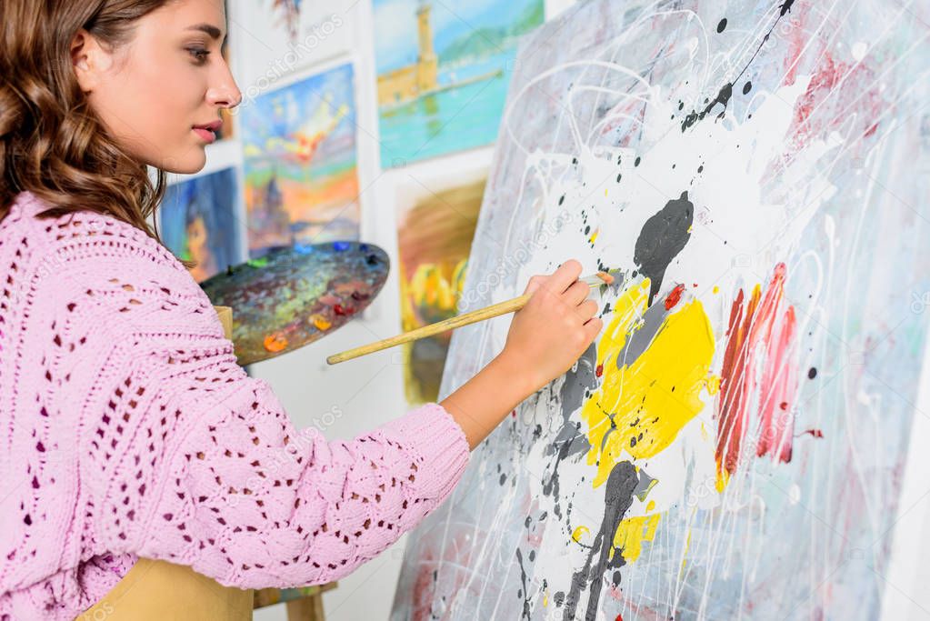 side view of attractive female artist painting in workshop