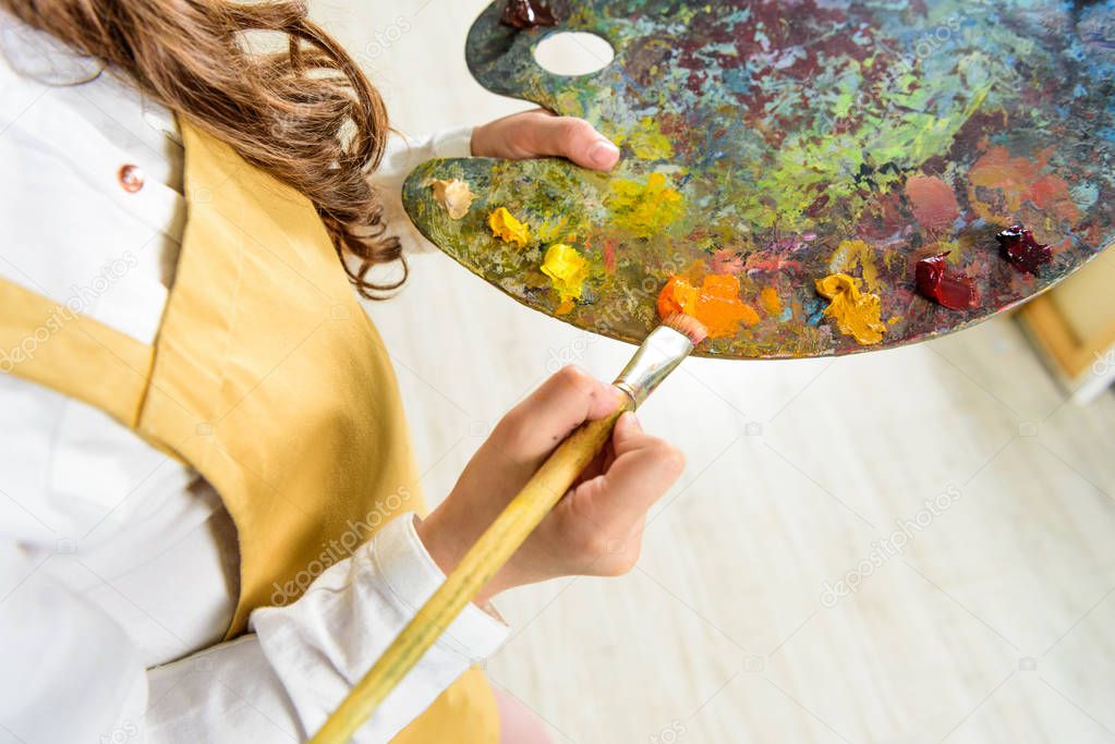 cropped image of kid taking oil paints from palette in workshop of art school