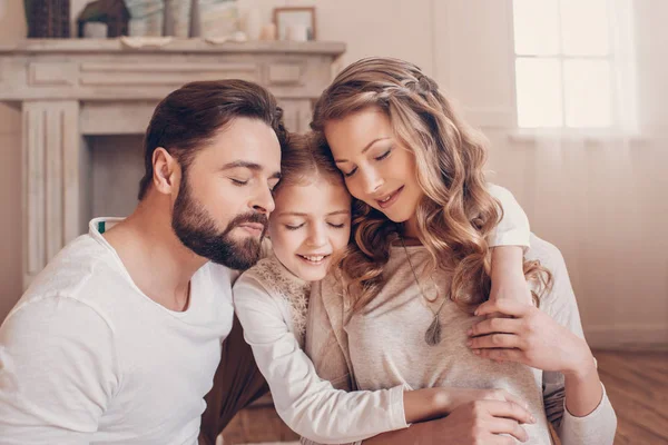 Familia joven y feliz con un niño sentado abrazándose juntos en casa - foto de stock