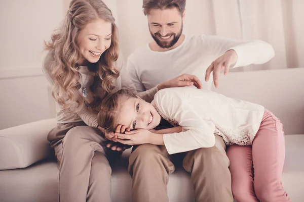 Pequeña hija feliz acostada en el regazo de los padres y mirando a la cámara - foto de stock