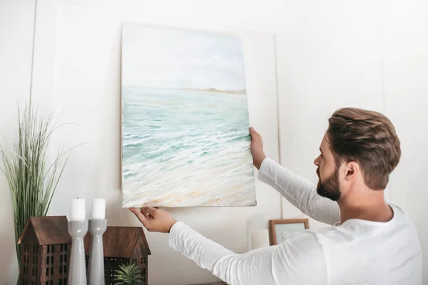 Joven barbudo colgando imagen en la pared en casa - foto de stock