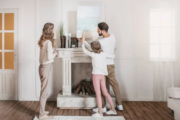 Feliz familia colgando foto de mar sobre la chimenea en casa - foto de stock
