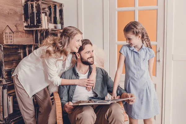 Hija, madre y padre sentado en mecedora y libro de lectura - foto de stock