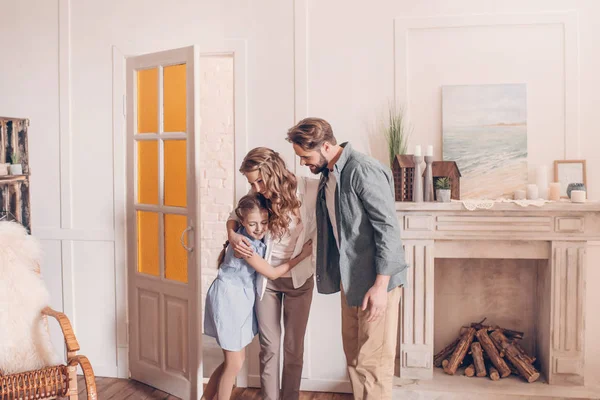 Familia feliz abrazando y de pie en casa con chimenea detrás - foto de stock