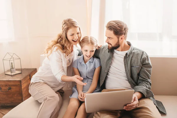 Familia feliz sentado en el sofá y el uso de la computadora portátil en casa - foto de stock