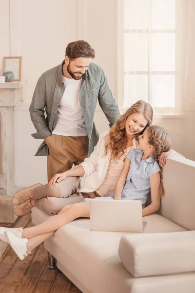 Happy family sitting on sofa and using laptop at home — Stock Photo
