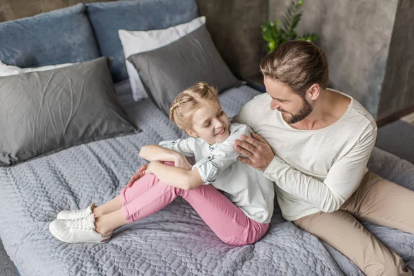 Feliz adorable hija y padre sentado en la cama en casa - foto de stock