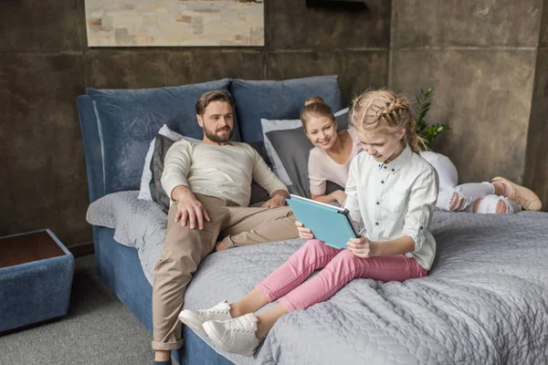 Entzückende Tochter nutzt digitales Tablet und liegt mit ihren Eltern im Bett — Stockfoto