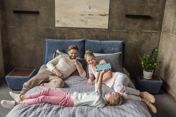 Entzückende Tochter nutzt digitales Tablet und liegt mit ihren Eltern im Bett — Stockfoto